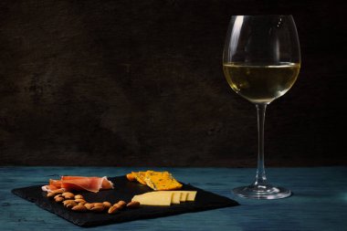 Mavi ve koyu arka plan, beyaz şarap ile kayrak bir tepsi Snacks. Peynirler, fındık, prosciutto. İşleme, boşluk yazar
