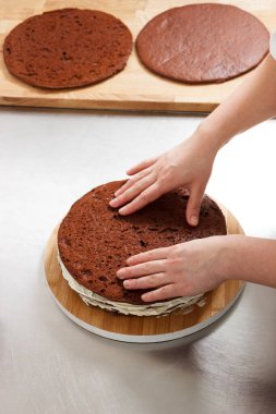 Woman is preparing chocolate cake with milk cream. The process of making the chocolate cake, from begin to the end. Made by hands for confectionery.