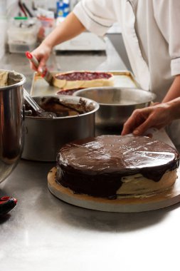 Woman smears chocolate cake with glaze icing, final stage of cooking. The process of making the chocolate cake, from begin to the end. Made by hands for confectionery.