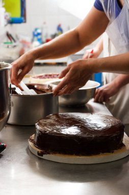 Woman smears chocolate cake with glaze icing, final stage of cooking. The process of making the chocolate cake, from begin to the end. Made by hands for confectionery.