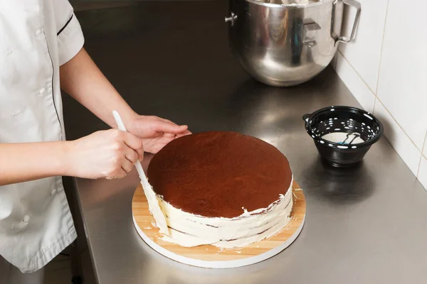 Woman is preparing chocolate cake with milk cream. The process of making the chocolate cake, from begin to the end. Made by hands for confectionery.