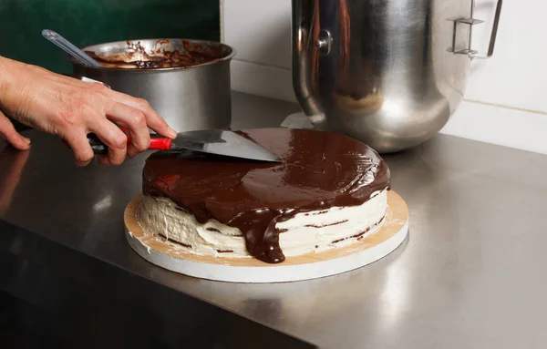 Woman smears chocolate cake with glaze icing, final stage of cooking. The process of making the chocolate cake, from begin to the end. Made by hands for confectionery.