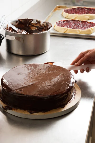 Woman smears chocolate cake with glaze icing, final stage of cooking. The process of making the chocolate cake, from begin to the end. Made by hands for confectionery.