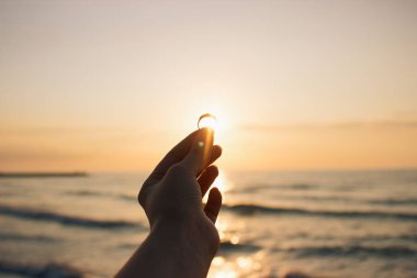Denizde gün doğumunda nişan yüzüğünü elinde tutan kadın. İtalya sahilinde evlenme teklifi. Film efekti, fotoğraf yazma işlemi