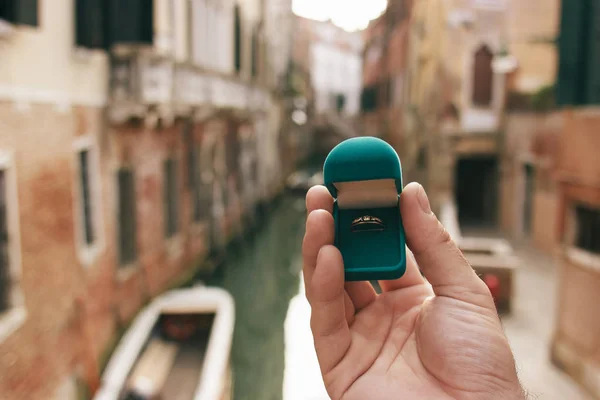 Homem segurando uma caixa azul com anel de noivado frente canal veneziano. Uma oferta de casamento em Veneza, Itália. Efeito de filme, processamento de autor de foto . Imagem De Stock