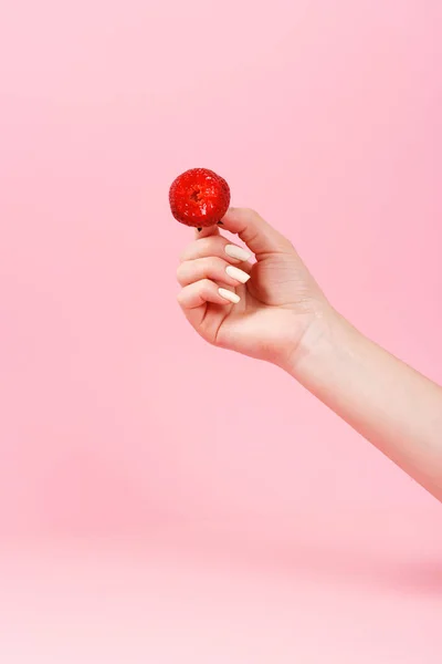 stock image A woman holds a bitten strawberry in her hand on a light green background.
