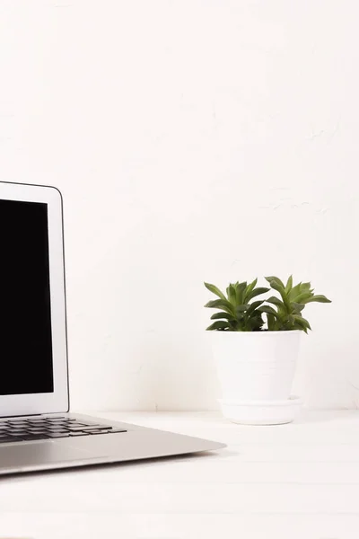 Egy laptop fekete képernyővel egy fehér asztalon egy zamatos háttér fehér fal Jogdíjmentes Stock Fotók