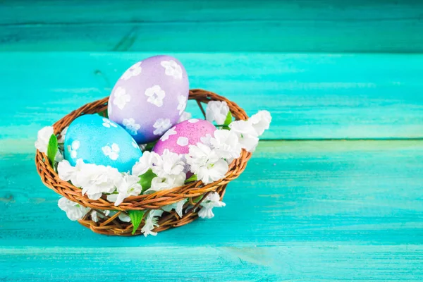 Violet and blue easter eggs in a basket with flowers. Blue wooden background. Happy easter.