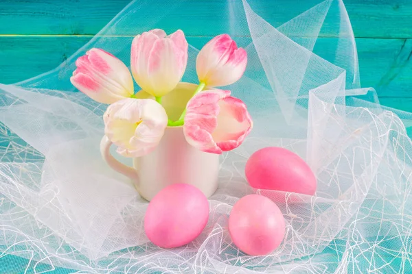 Roze paaseieren en tulpen in een vaas op witte stof en blauwe houten achtergrond. Stockfoto