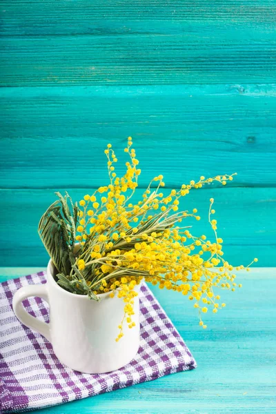 Flores amarillas de primavera de mimosa en una taza blanca sobre un fondo de madera azul . — Foto de Stock