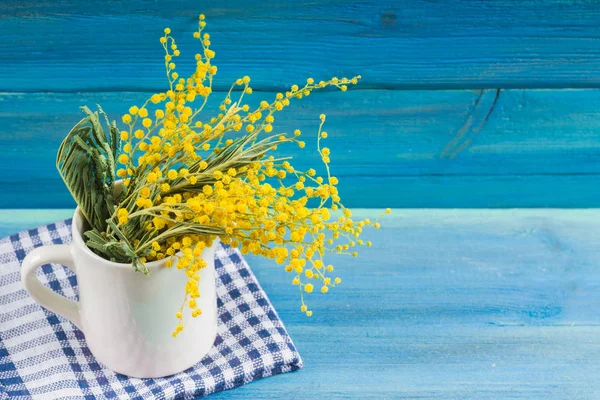 Flores amarillas de primavera de mimosa en una taza blanca sobre un fondo de madera azul . — Foto de Stock