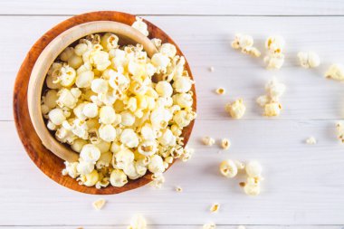 Ahşap bir bardak tuzlu patlamış mısır üzerinde beyaz bir tablodur. Patlamış mısır kase yatıyor. Üstten Görünüm.