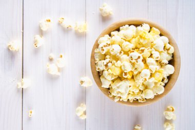 Ahşap bir bardak tuzlu patlamış mısır üzerinde beyaz bir tablodur. Patlamış mısır kase yatıyor. Üstten Görünüm.