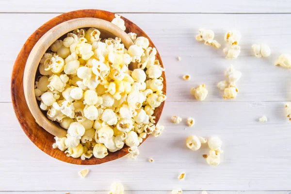 Slaný popcorn v dřevěných pohárech je na bílém stole. Popcorn se nachází kolem mísy. Pohled shora. — Stock fotografie