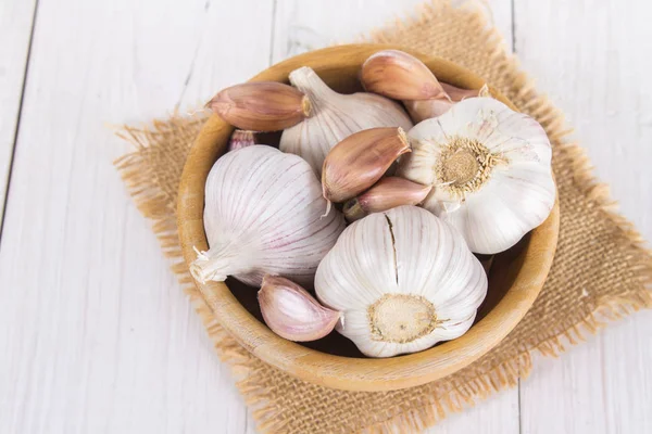 Garlic cloves and garlic bulb in a bowl on a white wooden table. — Stock Photo, Image