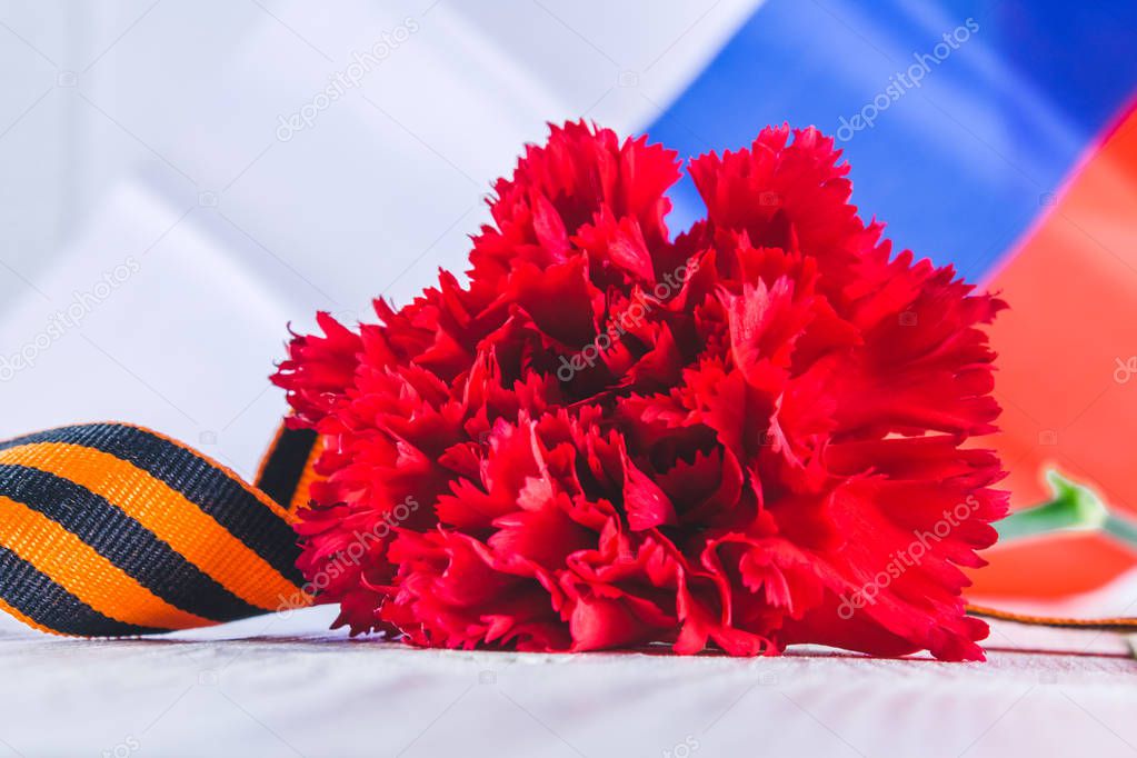 Carnation and ribbon of St. George, as a symbol of victory against the background of the Russian flag. May 9, the day of victory.