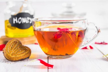 Bir fincan çay, bisküvi, konserve bal arka planda ve siyah bitkisel çiçek çay beyaz ahşap bir masa üzerinde.