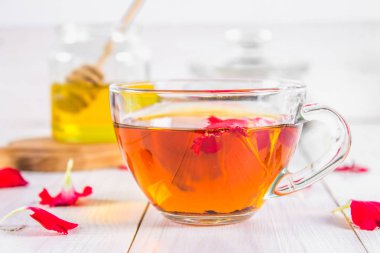 Bir fincan çay, bal ve bir kavanoz siyah bir bitki çiçek çayı ile bir banka beyaz ahşap bir masa üzerinde arka planda.