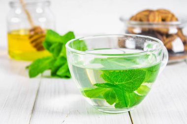 Nane çay bir fincan, bal kavanozu, bir beyaz tahta masada kurabiye.