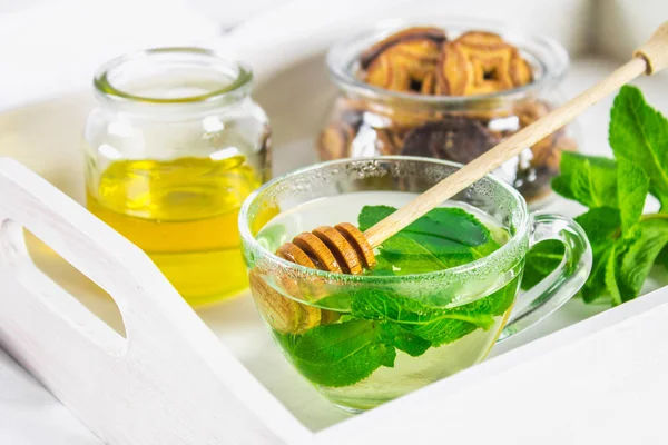 Té de menta en una taza, un frasco de miel, una galleta en un frasco, en una bandeja blanca en la cama . — Foto de Stock