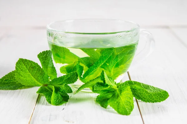 Beyaz ahşap bir masa üzerinde bir fincan nane çayı.