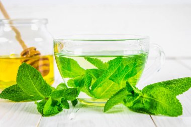 Bal kavanozu Beyaz ahşap bir masa üzerinde bir fincan nane çayı.