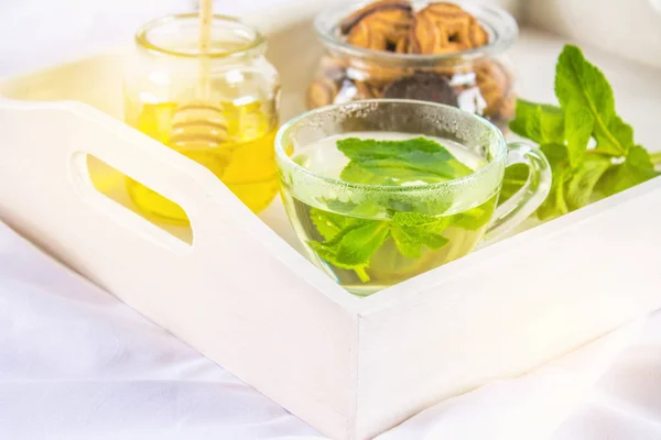 Pistáciová čaje v šálku, sklenice medu, cookie v jar, na bílém tácku v posteli. — Stock fotografie