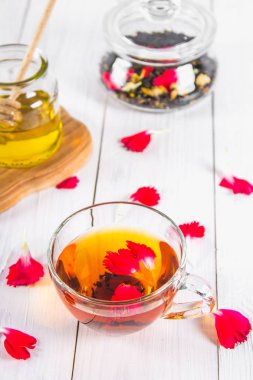 Bir fincan çay, bal konservesi ve siyah bir bitki çiçek çayı Beyaz ahşap bir masa üzerinde bir küptür. Üstten Görünüm.