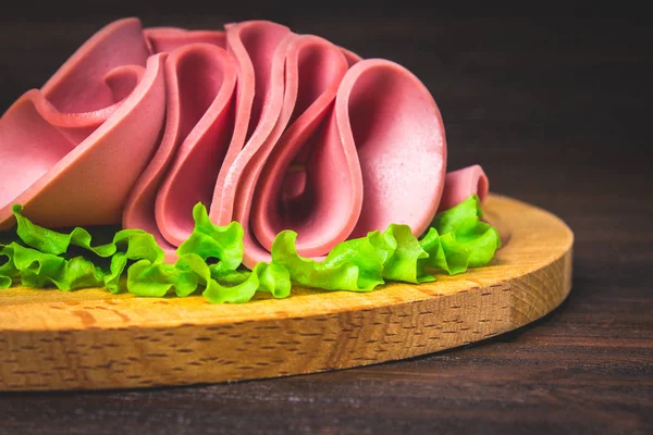 Salchicha en rodajas con ensalada sobre una tabla redonda de madera . —  Fotos de Stock