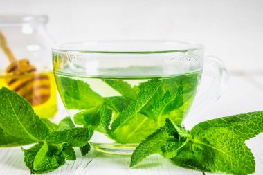 Bal kavanozu Beyaz ahşap bir masa üzerinde bir fincan nane çayı.