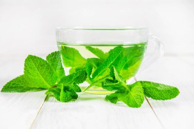 Beyaz ahşap bir masa üzerinde bir fincan nane çayı.