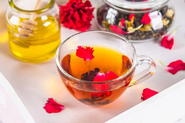 Een kopje thee, een blikje van honing en een potje zwarte kruidenthee op een — Stockfoto