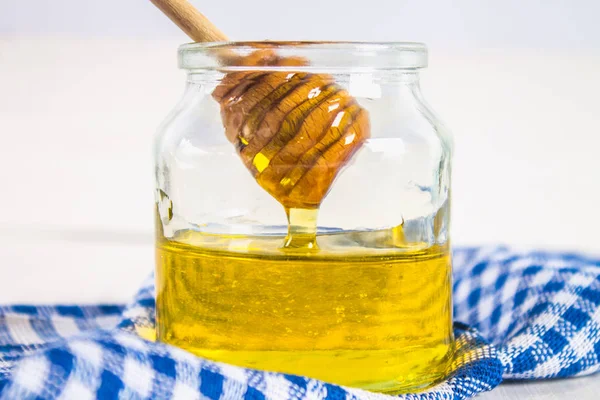 Mavi havlu ile beyaz bir tabloda bir kaşık bal kavanoz. Bir kaşık bal dökülür.