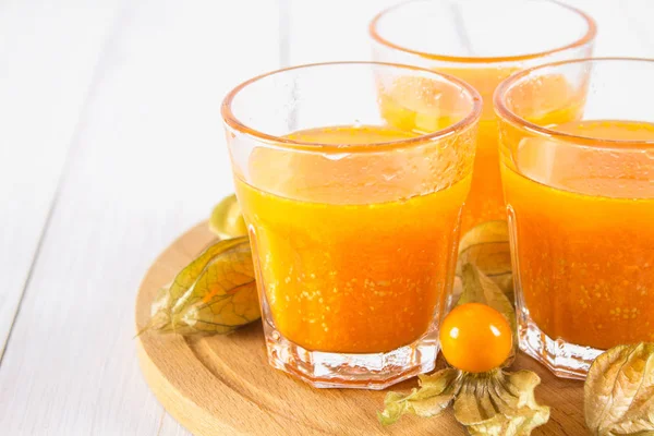 Un batido de naranja hecho de physalis sobre una mesa de madera blanca . — Foto de Stock