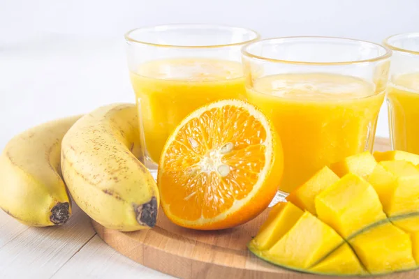 Sarı yüzlü mango, muz ve portakal bir beyaz tahta üzerinde ta