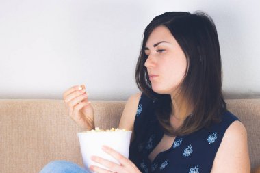 Bir kız kanepede televizyon izlerken ve patlamış mısır yemek. Üzüntü, depresyon duyguları vardır.