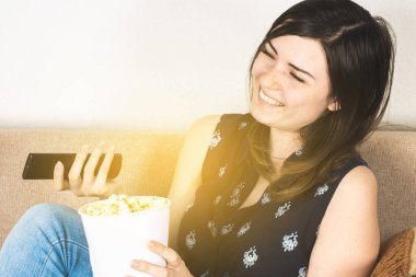 Bir kız kanepede televizyon izlerken ve patlamış mısır yemek. Duygular vardır kahkaha, sevinç, mutluluk.