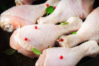 Ahşap bir masa üzerinde bir tavada çiğ tavuk budu. Yemek pişirmek için et malzemeler.