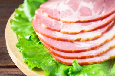 Taze yeşil salata ile dilimlenmiş jambon yuvarlak kesme tahtası üzerinde bırakır. Et ürünleri bir kahverengi ahşap tablo.