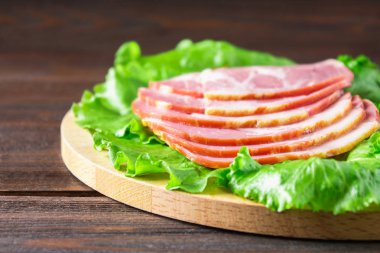 Taze yeşil salata ile dilimlenmiş jambon yuvarlak kesme tahtası üzerinde bırakır. Et ürünleri bir kahverengi ahşap tablo.