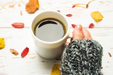 Bir kadının elinde bir kazak örme bir eşarp ile ahşap bir masa üzerinde sonbahar ortamda sıcak kahve bir fincan kazak. Konfor, sıcaklık, rahat.