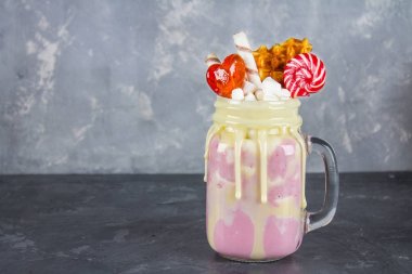 Pembe yüzlü, krem üzerinden Freakshake. Lolipop, waffle ve hatmi ile Monstershake. Bir Mason kavanoza aşırı milkshake. Koyu gri beton arka plan.