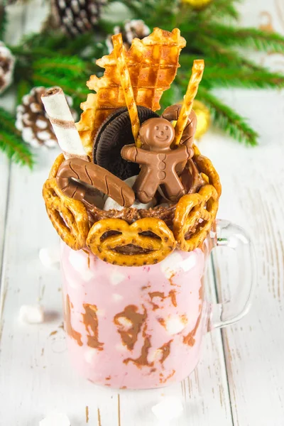 Frullato di frullato rosa, crema. Monstershake con un uomo cioccolato, canna, pretzel, biscotti, waffle e marshmallow. Frullato estremo in un barattolo di Mason. Tavolo in legno bianco. Atmosfera Capodanno, C — Foto Stock