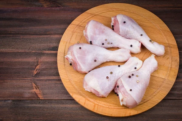 Raw chicken legs with bell pepper on a circular wooden board on