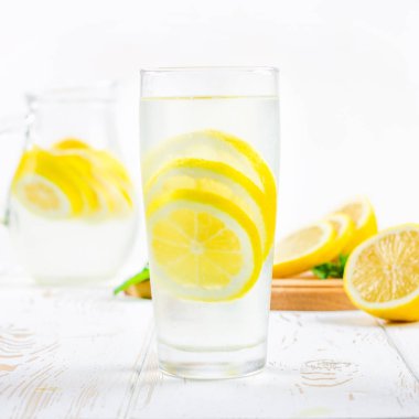 Bir cam kabı ve bir sürahi soğuk limonata limon tarafından çevrili beyaz ahşap zemin üzerinde.