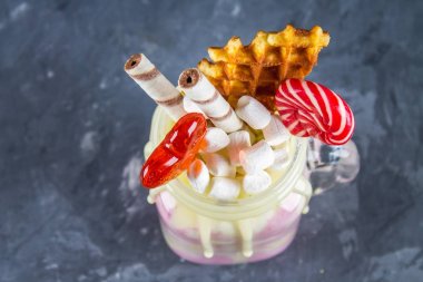 Pembe yüzlü, krem üzerinden Freakshake. Lolipop, waffle ve hatmi ile Monstershake. Bir Mason kavanoza aşırı milkshake. Koyu gri beton arka plan.