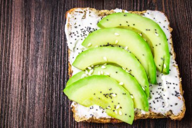 Ekmek dilimleri, zvezdami, avokado ve lor peynir kahverengi ahşap arka plan üzerinde kalpleri ile sandviç.