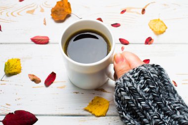 Bir kadının elinde bir kazak örme bir eşarp ile ahşap bir masa üzerinde sonbahar ortamda sıcak kahve bir fincan kazak. Konfor, sıcaklık, rahat.