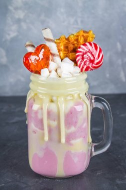 Pembe yüzlü, krem üzerinden Freakshake. Lolipop, waffle ve hatmi ile Monstershake. Bir Mason kavanoza aşırı milkshake. Koyu gri beton arka plan.