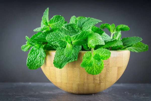 Yeşil nane gri bir arka plan üzerinde bir ahşap kase